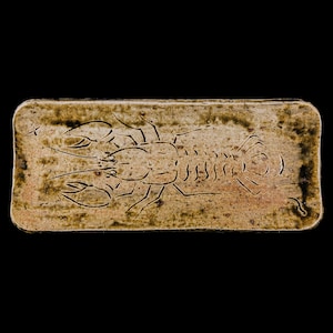 May include: A rectangular ceramic tile with a brown glaze. The tile features a raised design of a lobster in the centre.