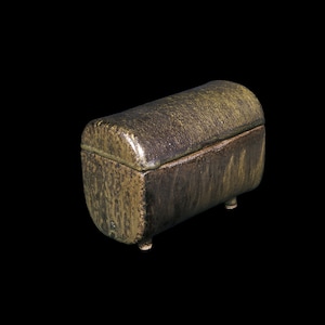 May include: A small, ceramic box with a rounded lid and a textured, green and brown glaze. The box has four small feet.