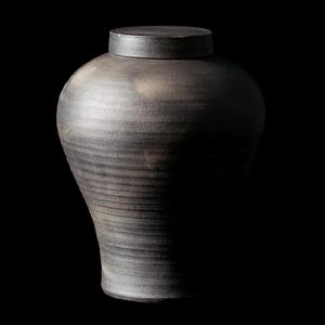 Peut inclure: Un pot en céramique noire avec un couvercle. Le pot a un corps lisse et arrondi et une ouverture légèrement évasée. Le couvercle est plat et a un bord légèrement surélevé.