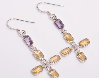 May include: A pair of silver drop earrings. Each earring has a rectangular purple gemstone at the top, followed by yellow rectangular gemstones in a cross formation. The earrings are displayed against a white backdrop.