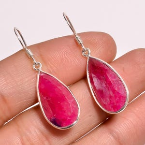 May include: A pair of silver drop earrings. Each earring features a large, faceted, teardrop-shaped, hot pink gemstone set in a silver bezel, suspended from silver ear wires.