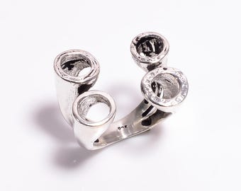 May include: A silver ring with a unique design featuring four circular, hollow elements. The ring has a modern, abstract style, with a polished finish. The ring is a statement piece of jewelry.