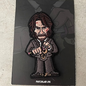 Może przedstawiać: Haftowana naszywka przedstawiająca stylizowaną postać z kreskówki z brązowymi włosami i brodą, ubraną w ciemny garnitur. Postać trzyma złoty przedmiot. Naszywka ma czarną obwódkę i tekst "PATCHLAB.DE" na dole.
