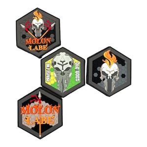 May include: A collection of five black, gray, and orange hexagon-shaped patches. Each patch features a skull design with text, including "MOLON LABE" and "PRAISE THE OLD GODS". The patches have a textured appearance.