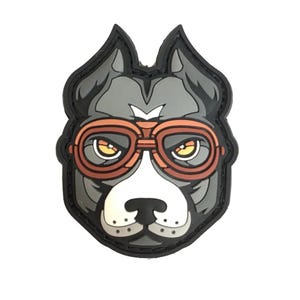 以下が含まれることがあります： 黒と灰色の漫画の犬が茶色のゴーグルをかけています。犬の目は黄色で、ゴーグルは赤いフレームです。
