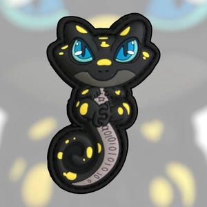 May include: A black gecko-shaped patch with striking blue eyes and yellow markings. The gecko's tail features a binary code design. This patch is designed to be attached to items like clothing or bags, and is made of a durable material.