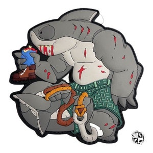 Op de afbeelding: Een grijze haaienkarakterpatch met een gespierd lichaam, een groene korte broek en een haak. De haai wordt afgebeeld met rode bloeddetails en eet een blauw object. De patch heeft een zwarte rand.