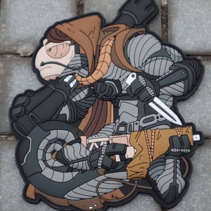 May include: A detailed patch featuring a futuristic warrior in gray and black armor, holding a knife and a weapon. The warrior has a brown hood and a tan-colored jacket. The patch is designed with a 3D effect.