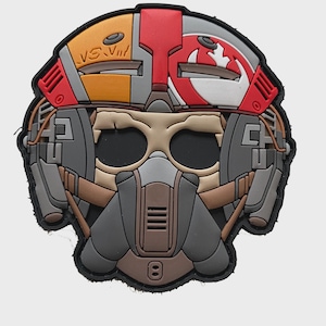 Peut inclure: Un écusson représentant un casque de pilote stylisé. Le patch est principalement gris, marron, rouge et jaune, avec un aspect détaillé et superposé. Le design comprend le texte "VS. VII" et un emblème circulaire.