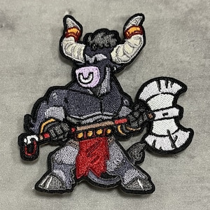 May include: Embroidered patch depicting a minotaur warrior with a stern expression, holding a battle axe. The minotaur has grey and black armour, a red loincloth, and large horns. The patch is outlined in black.
