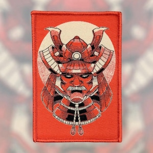 May include: Embroidered patch featuring a detailed illustration of a samurai helmet and face in shades of red and black. The design is set against a white circle and a red rectangular background. The patch has a stitched border.