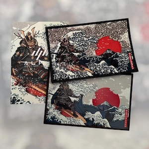 Könnte beinhalten: Drei Aufnäher und eine Karte mit einem Samurai-Krieger, der auf einer Welle surft. Die Aufnäher haben einen schwarzen Rand und eine rote Sonne im Hintergrund. Auf der Karte stehen die Worte "ALPHA" und "GRAPHIC SKETCH ILLUSTRATION".