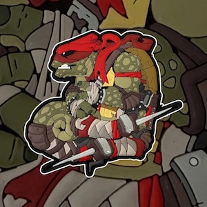 Può includere: Immagine di Raphael delle Tartarughe Ninja, in stile cartoon. Il personaggio è raffigurato in verde, marrone e rosso, con una bandana rossa, che tiene due sai. L'immagine ha un bordo bianco e uno sfondo strutturato.