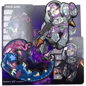 Peut inclure: Deux cartes de personnage illustrées pour un jeu. La première carte représente un extraterrestre spatial violet avec un pistolet et le texte "SPACE ALIEN". La deuxième carte représente un extraterrestre spatial violet avec un pistolet et le texte "DINE".