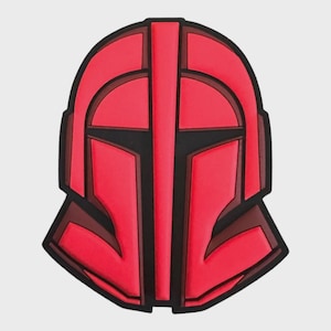 Pode incluir: Acessório em forma de capacete vermelho e preto. O design apresenta um capacete estilizado com uma linha vertical central e formas angulares. O esquema de cores é principalmente vermelho com detalhes em preto, criando uma aparência ousada e gráfica.