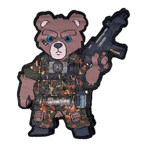May include: Embroidered patch featuring a brown bear with blue eyes, a scar, and an angry expression. The bear is dressed in camouflage military gear and holding a black rifle. The patch has a black border.