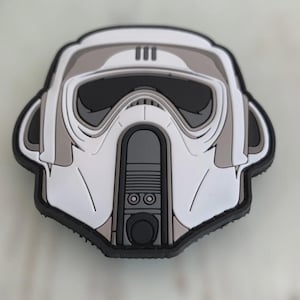 Può includere: Una toppa bianca, grigia e nera con un design stilizzato del casco di un soldato delle tempeste. La toppa ha un aspetto dettagliato e stratificato con un bordo nero. La visiera del casco è nera e il design include accenti grigi e bianchi.