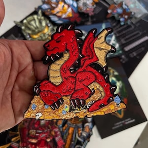 May include: Embroidered patch of a red dragon on a pile of gold coins, jewels, and skulls. The dragon has gold wings and a detailed design. The patch is designed for clothing or accessories.