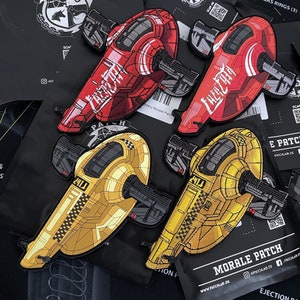 May include: Three embroidered patches featuring a futuristic vehicle design. The patches are in red, gold, and yellow with black outlines. The patches have the text "2414" and "PATCHLAB.DE" printed on them.