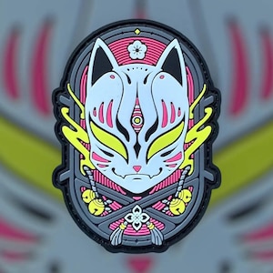 May include: A gray, black, pink, and yellow embroidered patch with a stylized fox mask design. The mask has a white background with pink and yellow details. The patch is surrounded by a gray border with a pink and yellow floral design.