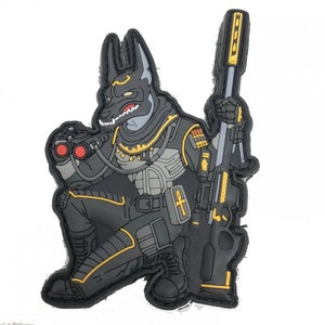 May include: A black patch depicting Anubis in tactical gear, kneeling and holding a sniper rifle. The Anubis figure has a canine head, wearing a helmet and body armour with gold accents. The patch also includes binoculars, and is a detailed design.