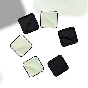 May include: A selection of black and white square patches, each displaying a different weapon design. The patches feature images of knives, a gun, and other tactical gear. The patches are arranged in a circular pattern against a white backdrop.
