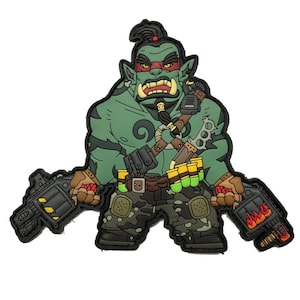 Könnte beinhalten: Ein grüner Cartoon-Orc-Charakter-Aufnäher mit rotem Stirnband, der zwei schwarze Waffen hält. Der Orc trägt eine Camouflage-Hose und einen braunen Gürtel mit gelben und grünen Akzenten. Der Aufnäher hat eine schwarze Umrandung.