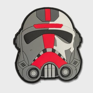 Pode incluir: Um patch com um design de capacete estilizado em tons de cinza, branco, preto e vermelho. O capacete tem um design geométrico detalhado com uma faixa vermelha no centro e uma borda preta. O patch é provavelmente para um fã de ficção científica.