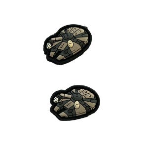 May include: Two black and gray rubber patches of the Millennium Falcon spaceship from Star Wars.