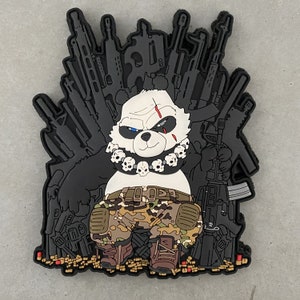 May include: A black and white panda bear wearing a camouflage outfit and a skull necklace sits on a throne made of guns. The panda is holding a gun in its right hand.