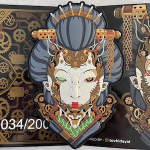 May include: A detailed patch featuring a geisha with a steampunk aesthetic. The design incorporates gears, metallic accents, and a robotic eye. The geisha's hair is grey, and the face has a mix of mechanical and human features. The patch is numbered 034/200.