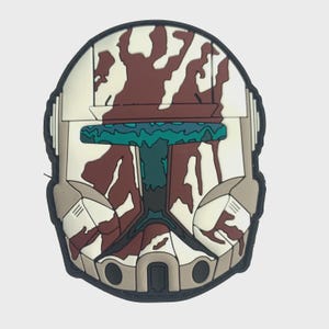 Può includere: Una toppa raffigurante un casco stilizzato con base bianca, motivi mimetici marroni e dettagli turchese. La toppa ha un bordo nero e un design simmetrico dettagliato.