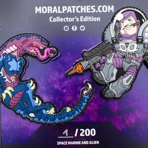 May include: Two embroidered patches, one of a purple alien with a pink tongue and the other of a space marine with a gun and a cigar. The patches are on a purple background with stars. The text "1/200 SPACE MARINE AND ALIEN" is below the patches.