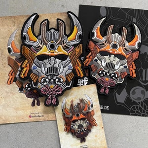 May include: Embroidered patches with a samurai helmet design in orange, grey, and yellow. The patches have a black border and Japanese text. The design is repeated on several patches and a small pin.