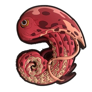 Puede incluir: Un parche rojo y marrón con forma de pulpo y borde negro. El diseño presenta una criatura estilizada con una cabeza grande, un ojo y tentáculos. El parche tiene un aspecto texturizado y probablemente está hecho de goma o un material similar.