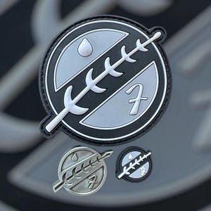 Peut inclure: Un patch noir et blanc avec une image stylisée d'une plante et une goutte d'eau. Le patch a un numéro "7" blanc au centre. Il existe deux versions plus petites du patch, une en noir et blanc et une en argent.