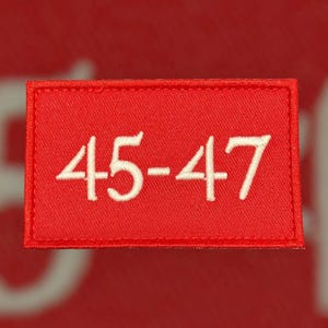 May include: Red fabric patch with white embroidered text that reads "45-47".