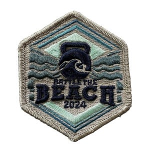 May include: Embroidered patch in a hexagonal shape. The design features a kettlebell and waves in shades of blue and teal, with the text "BATTLE THE BEACH 2024". The patch has a light gray border.