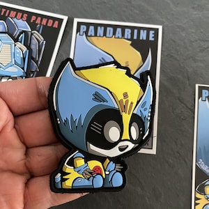 May include: A cartoon-style patch featuring a Wolverine-inspired character with blue and yellow accents. The patch has a black border and is set against a dark background. The word "PANDARINE" is visible on a nearby card.