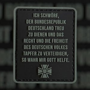 Puede incluir: Un parche rectangular con fondo gris oscuro y borde gris claro. El parche presenta texto en alemán y un emblema estilizado. El texto dice: "ICH SCHWÖRE, DER BUNDESREPUBLIK DEUTSCHLAND TREU ZU DIENEN..."