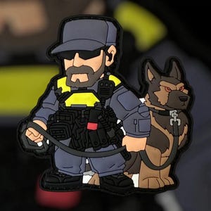 Può includere: Toppa in stile cartone animato raffigurante un agente delle forze dell'ordine con un pastore tedesco. L'ufficiale indossa un'uniforme blu, occhiali da sole e un giubbotto tattico. Il cane è marrone e nero. La toppa ha un bordo nero.