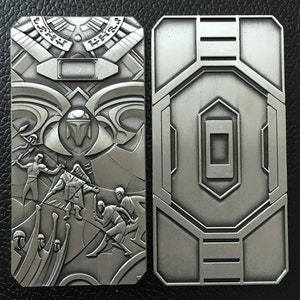 May include: Two silver metal plates with intricate designs. The left plate features a raised design of figures in a scene, while the right plate has a geometric pattern.