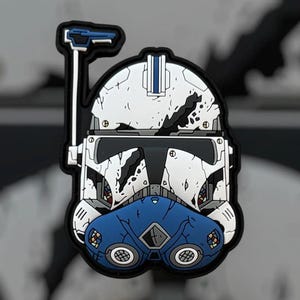 May include: A detailed, colorful patch featuring a white and blue helmet design with a black border. The helmet has a blue visor and a blue antenna-like structure. The design has a distressed, battle-worn aesthetic.