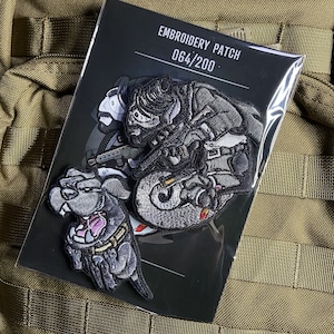 Może przedstawiać: Haftowane naszywki z postaciami z kreskówek w odcieniach szarości, czerni i różu. Jedna przedstawia psa, druga postać na motocyklu. Widoczny jest tekst "EMBROIDERY PATCH 064/200".