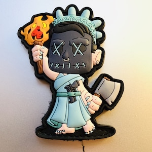 May include: A blue and white Statue of Liberty figurine with a black mask and X's for eyes. The figurine is holding a torch and an axe.