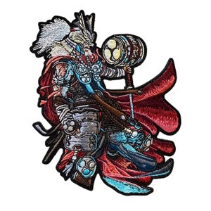 Puede incluir: Parche bordado con una ilustración detallada de una figura de guerrero con un martillo. El diseño incorpora tonos de rojo, azul, plata y blanco, con costuras intrincadas. El guerrero se representa en una pose dinámica, con una capa roja fluida.