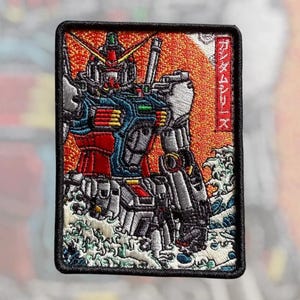 May include: A rectangular embroidered patch featuring a Gundam robot in red, blue, and silver threads against a bright orange sun background. The design includes stylized blue and white waves at the bottom and vertical Japanese text in a red border.