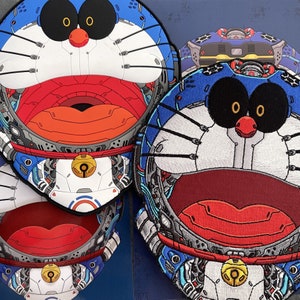 May include: Three embroidered patches featuring a cartoon character with blue and white details. The character has a large, red mouth and black eyes. The patches are made of a soft, textured fabric.