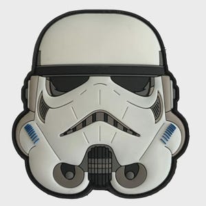 Peut inclure: Un design de casque de Stormtrooper blanc et noir. Le casque présente un design détaillé avec des accents noirs, des ombres grises et des détails bleus. Le casque est posé sur un fond gris clair.