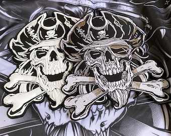 May include: Embroidered patches featuring a skull wearing a pirate hat, crossed bones, and a beard. The patches are black, white, and tan, with detailed stitching. The patches are designed with a pirate theme.